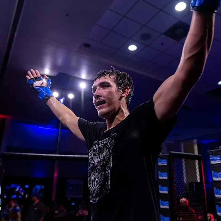 Ethan Riley raising his gloved arms inside the MMA cage